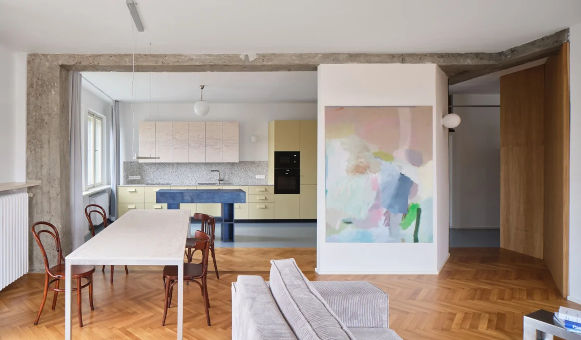Open-plan living area with original oak herringbone parquet flooring and exposed concrete structural beams in a Prague apartment.