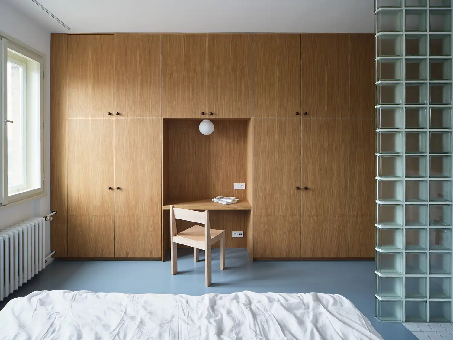 Full-height oak veneer wardrobe in a bedroom with an integrated recessed desk and a minimalist wooden chair.