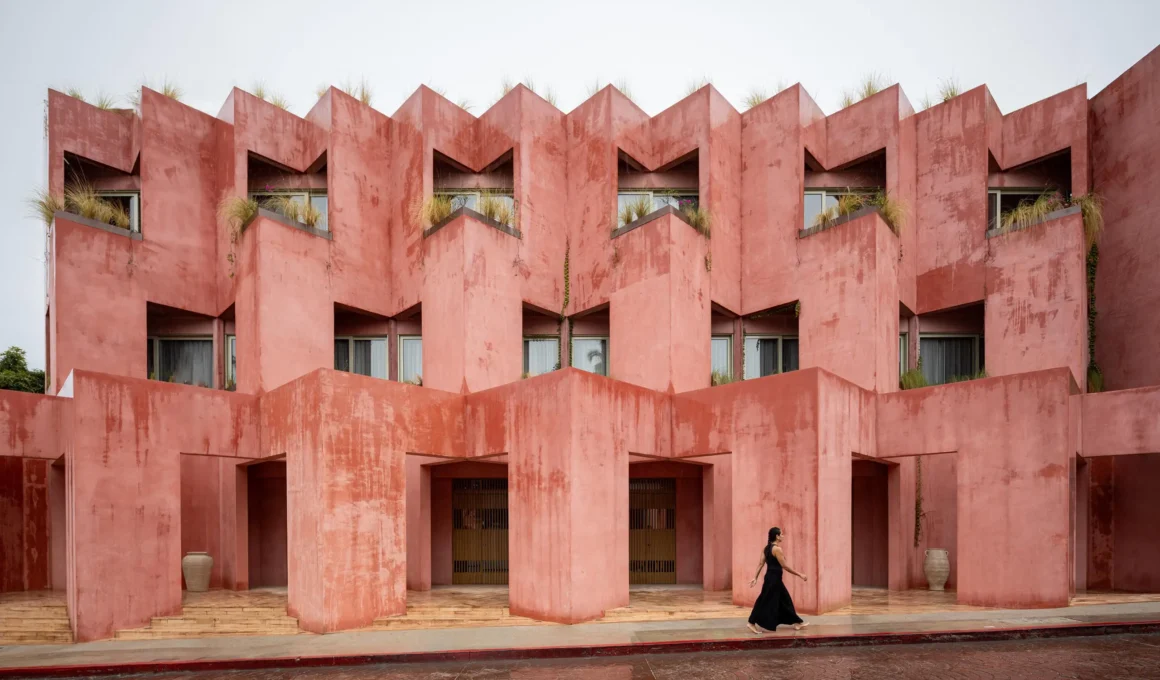 Frontal view of the pink stucco facade with rhythmic zig-zag window openings.