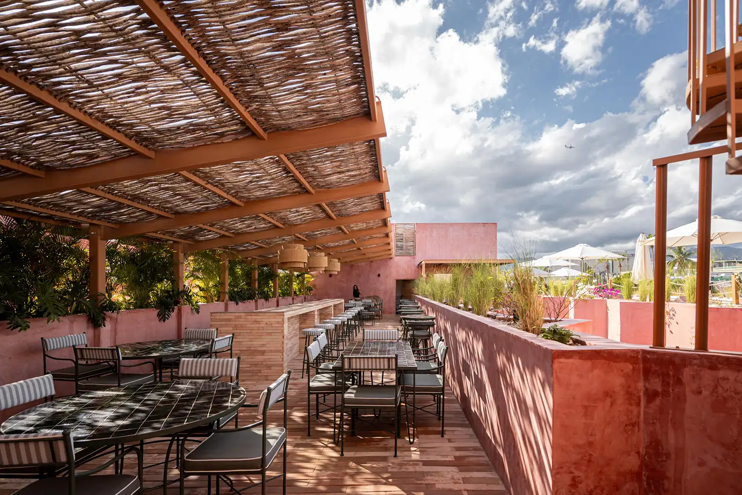 Rooftop bar area under a rustic woven wooden pergola.