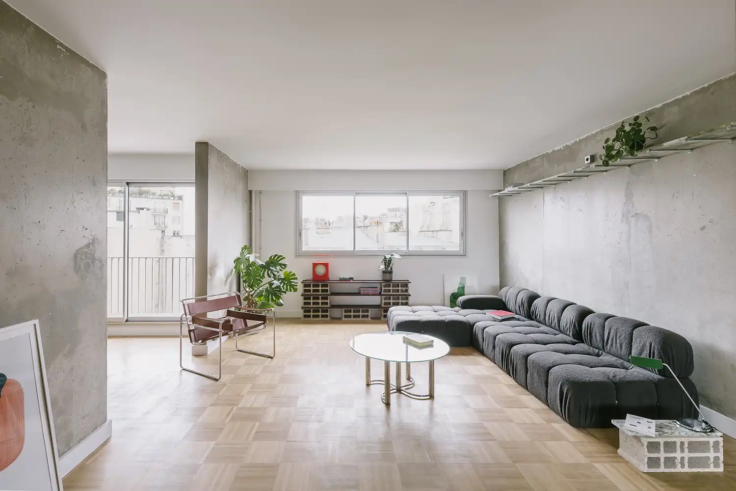 Spacious living room with large windows, a low-profile modular gray sofa, and a vintage leather armchair.