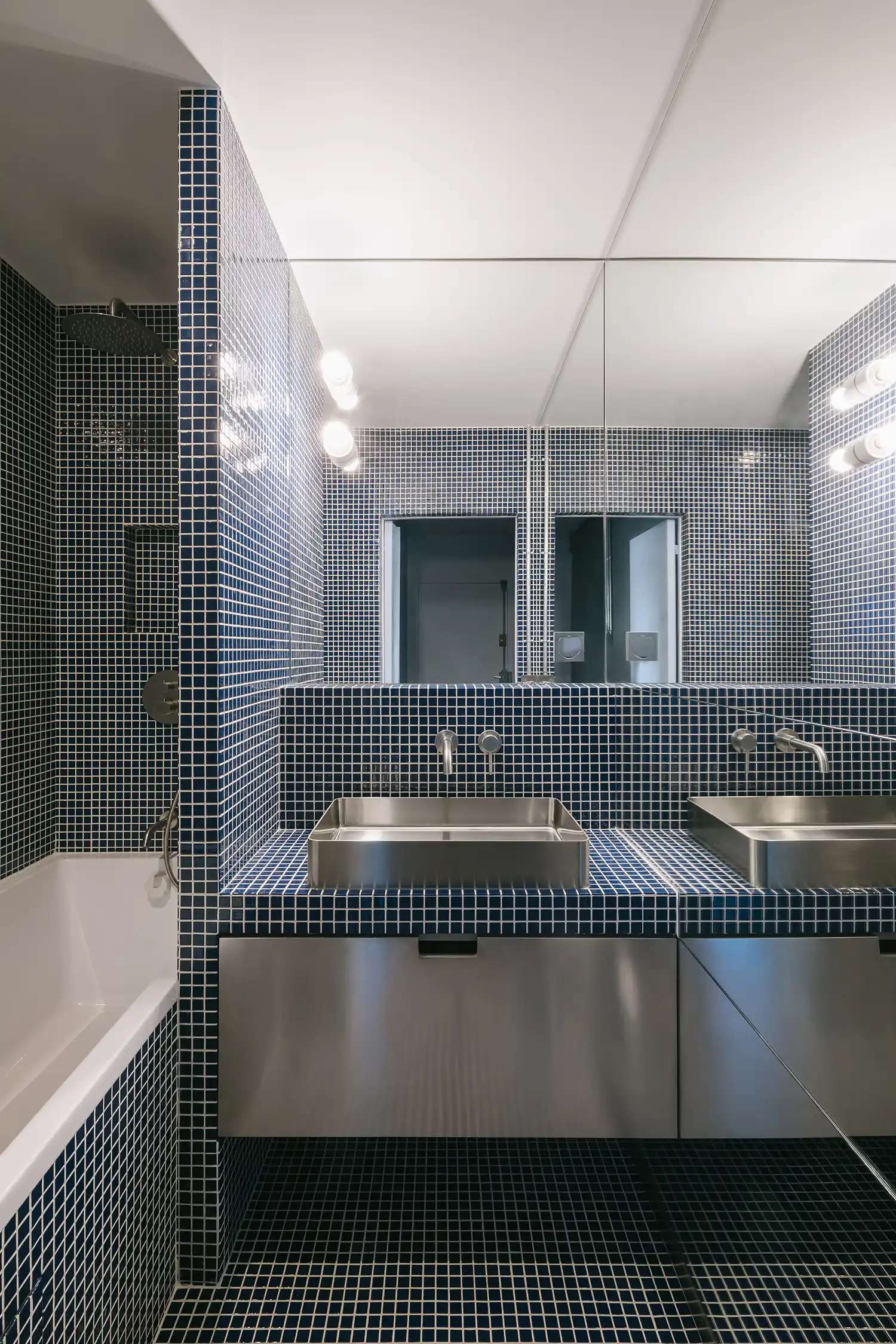 Contemporary bathroom with navy blue mosaic tiles, a large mirror, and a stainless steel trough sink.
