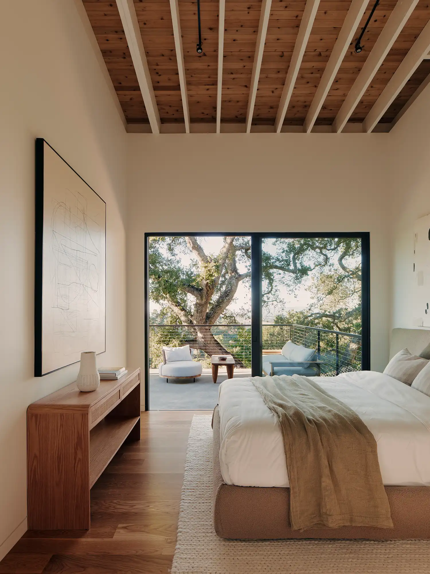 Bedroom with exposed wood ceiling beams and access to a private balcony among the trees.