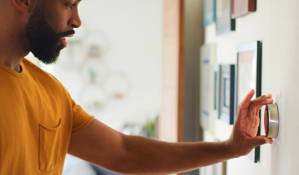 A person adjusting a modern smart thermostat on a wall to control home heating and reduce energy costs.