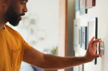 A person adjusting a modern smart thermostat on a wall to control home heating and reduce energy costs.