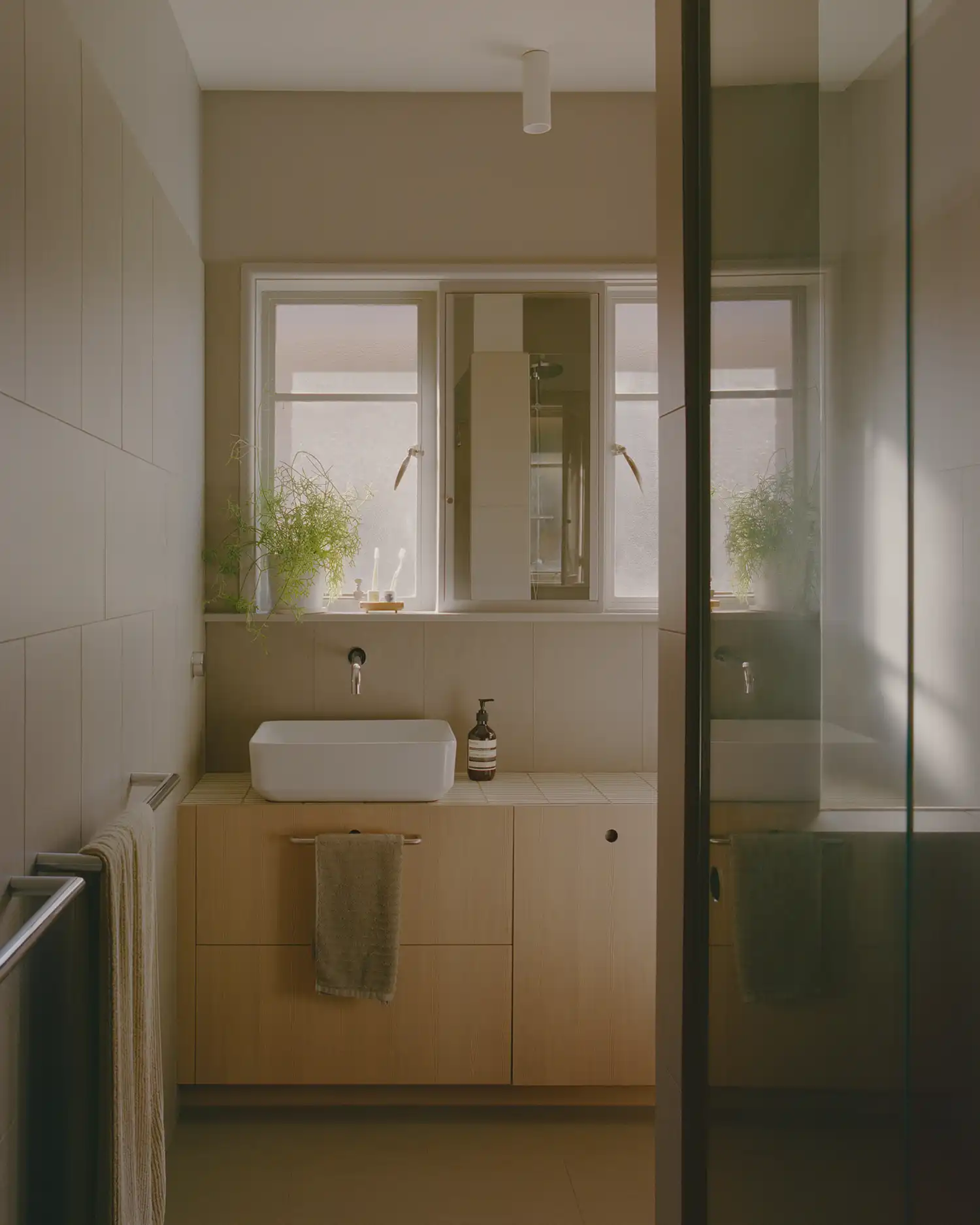 Modern bathroom in Cascade House with light timber vanity, white sink, and neutral wall tiles.