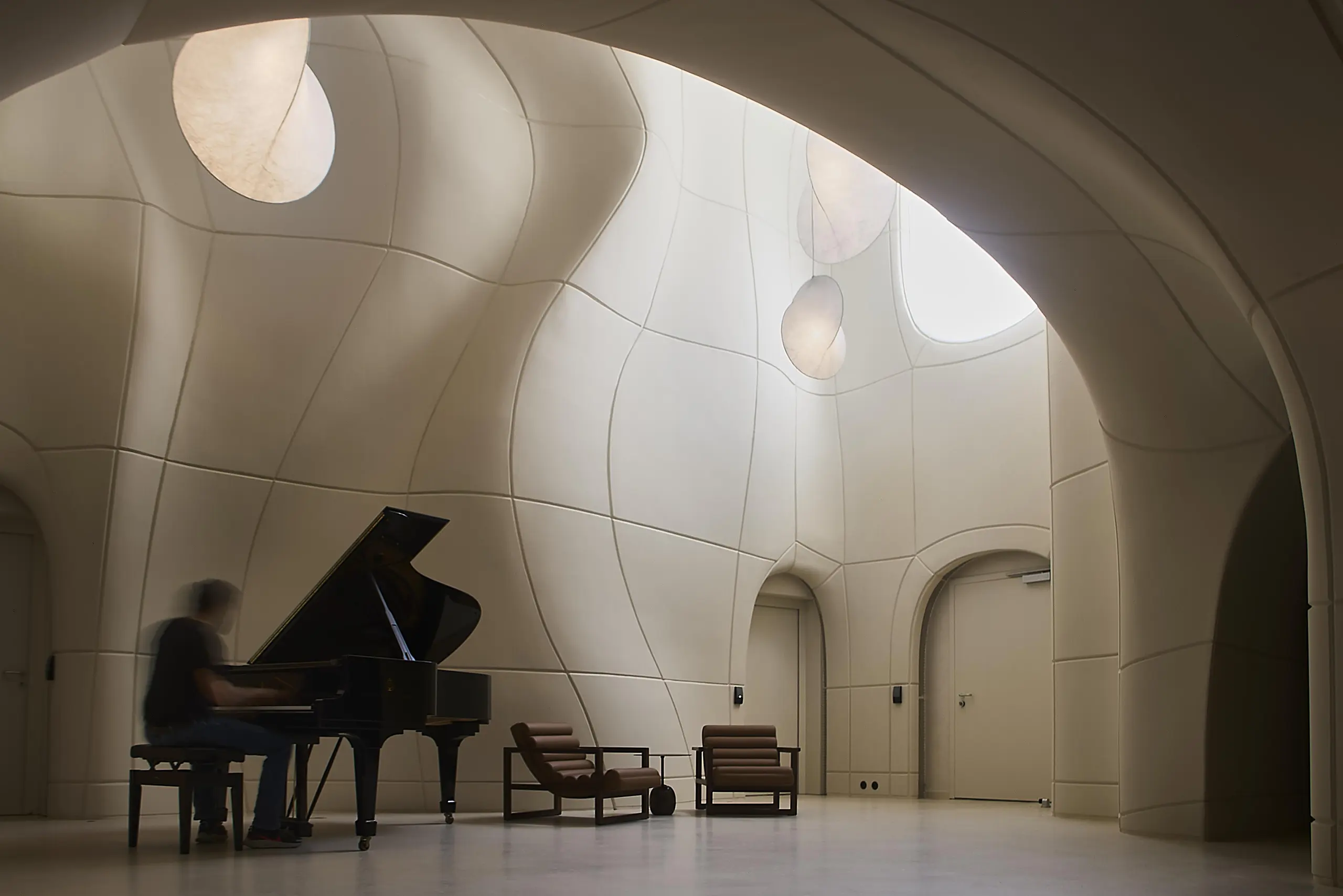 musician playing a grand piano in a white, organic-shaped room with curved GFRC walls.