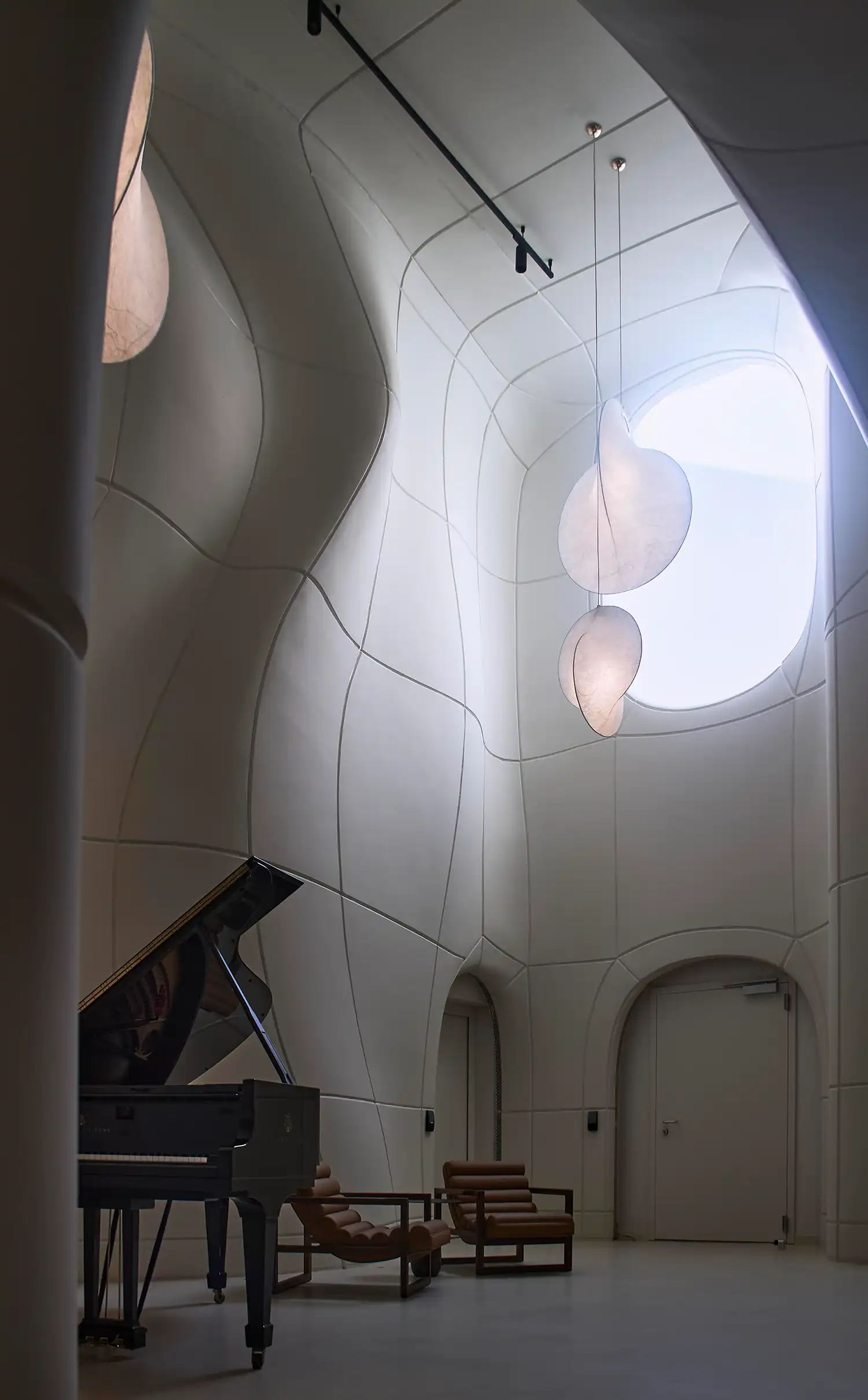 High-angle shot of a grand piano in a white sculptural atrium with organic light fixtures.