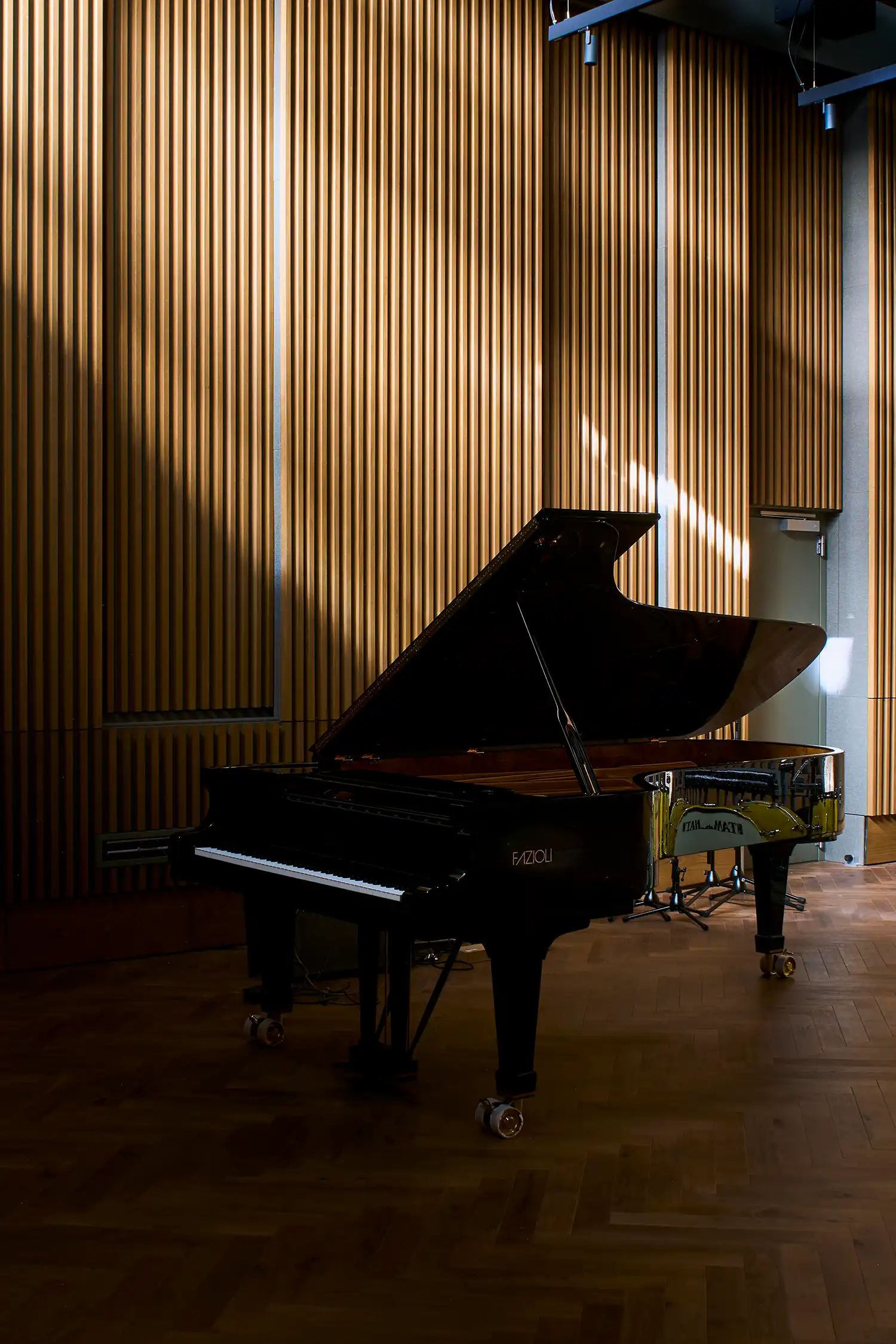 A black grand piano in a studio with vertical timber acoustic wall panelling and herringbone floors.