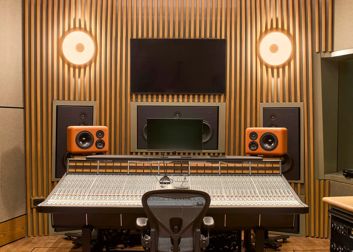 Professional mixing console in a studio with orange speakers and timber acoustic walls.