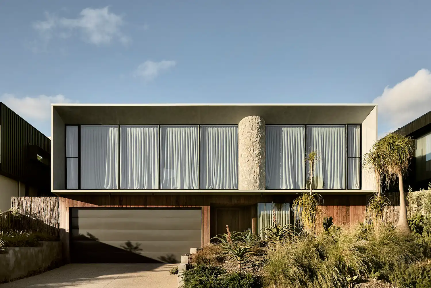 Symmetrical front elevation of a modern house with a large concrete cantilever and integrated limestone column.