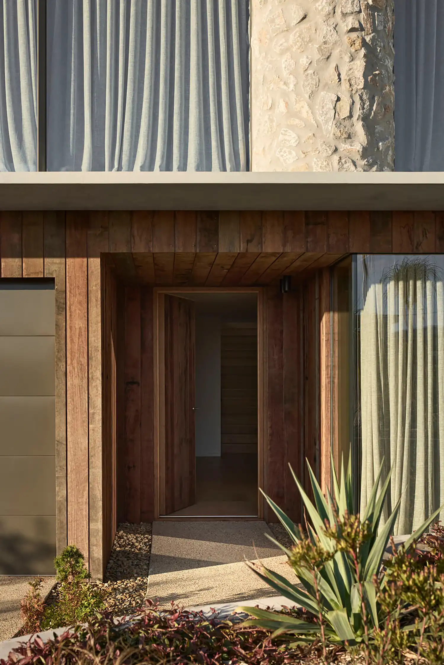 Close-up of a recessed timber entry door surrounded by native coastal succulents and greenery.