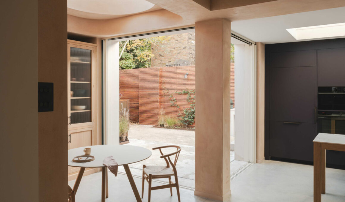 Modern open-plan dining area with clay plaster walls, a circular skylight, and a views of a timber-fenced garden.