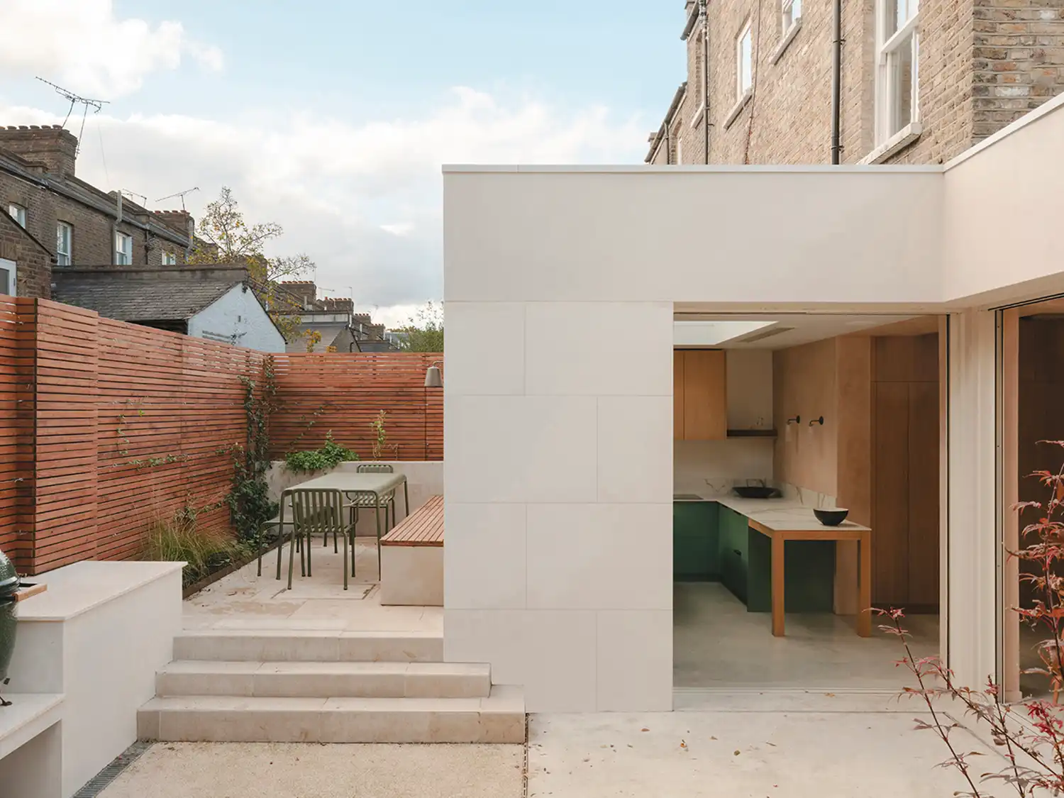 Rear exterior view of Balmore House featuring a Portland Stone extension and a sunken patio with a built-in bench.