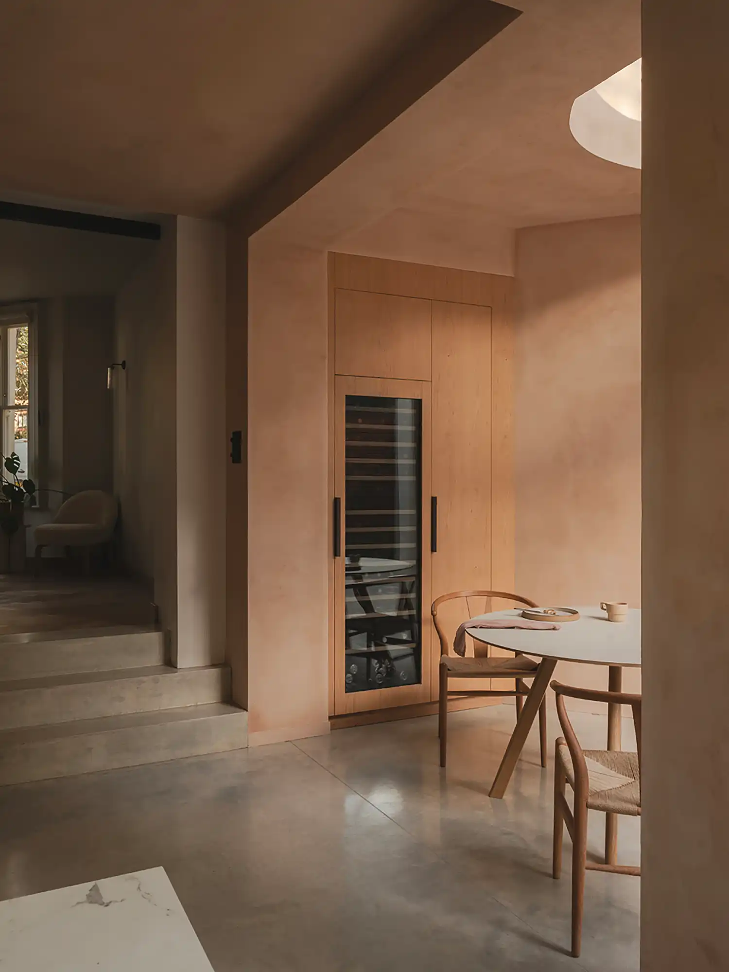 Living area with a wine fridge integrated into bespoke timber joinery next to a minimal dining setup.