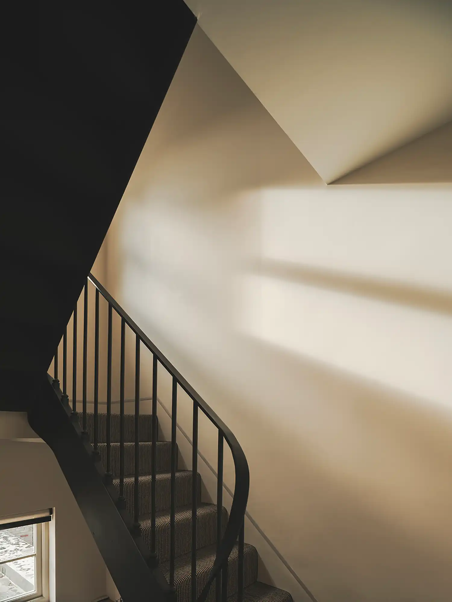 Minimalist staircase with a black metal banister and striped carpet under sharp geometric shadows.