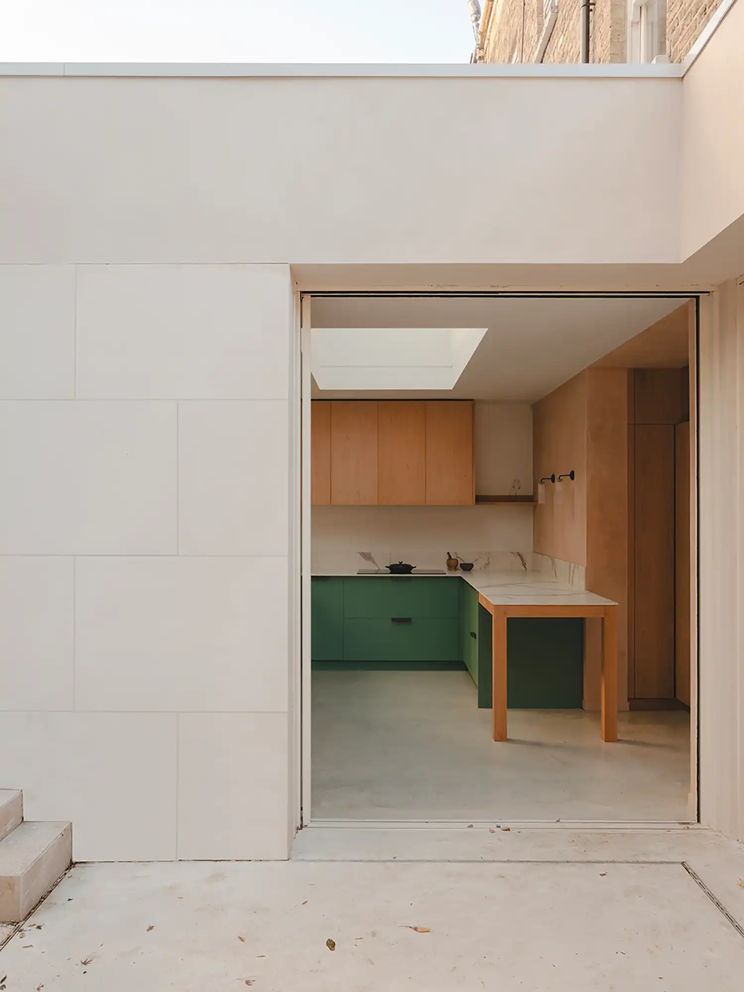 View from the patio looking into a kitchen with sage green lower cabinets and a wooden island table.