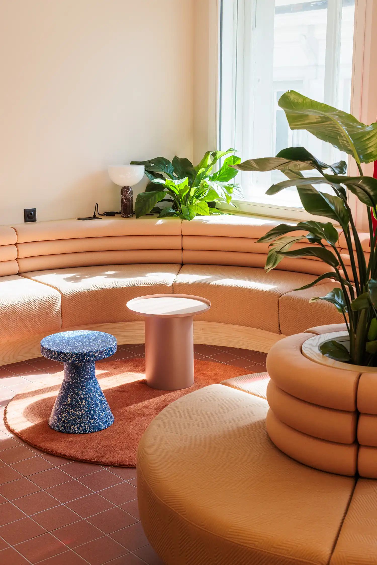 Curved modular seating in a sunlit corner with blue terrazzo-style stool