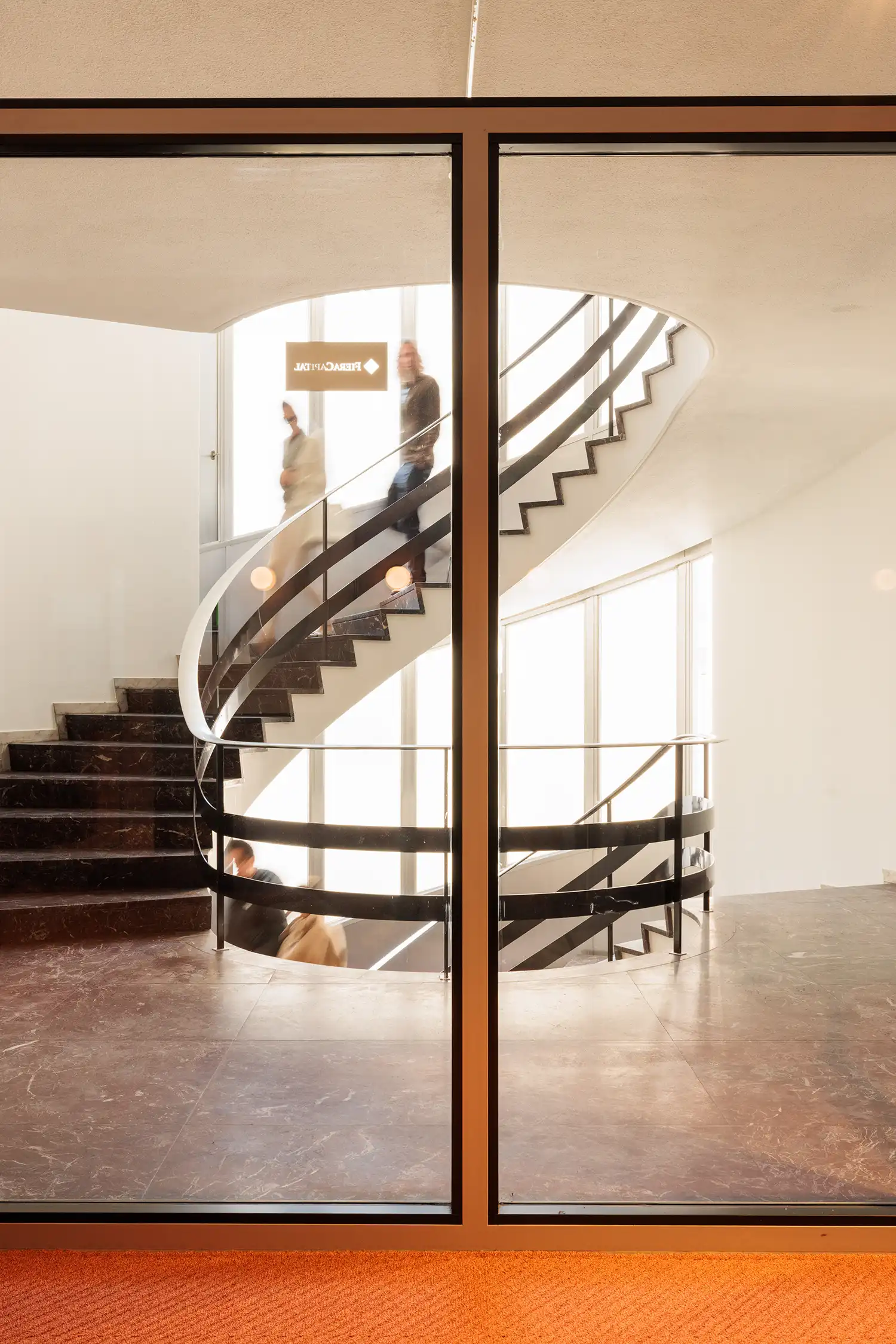 Spiral staircase with marble steps and dark metal railings behind glass