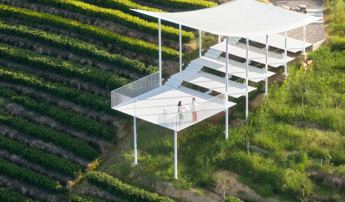 High-angle view of the Floating Pavilion showing its white stepped platforms and curved roof amidst green tea terraces.
