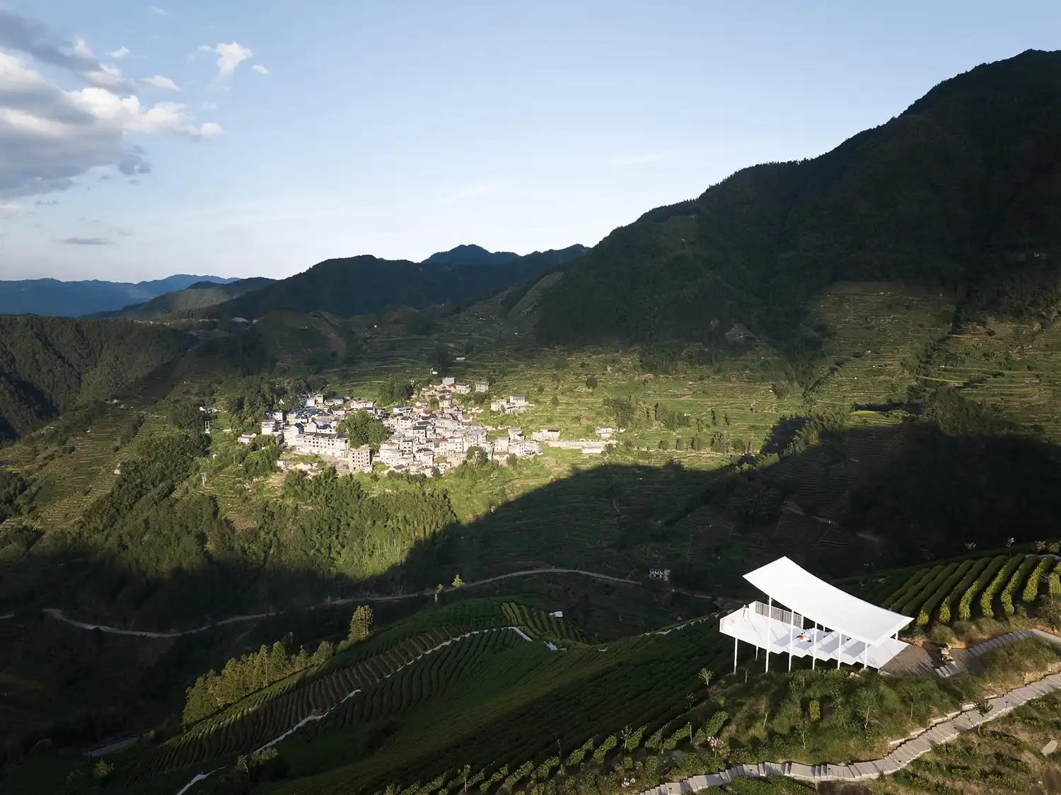 Wide aerial view of the Floating Pavilion overlooking a traditional village nestled in a mountain valley.