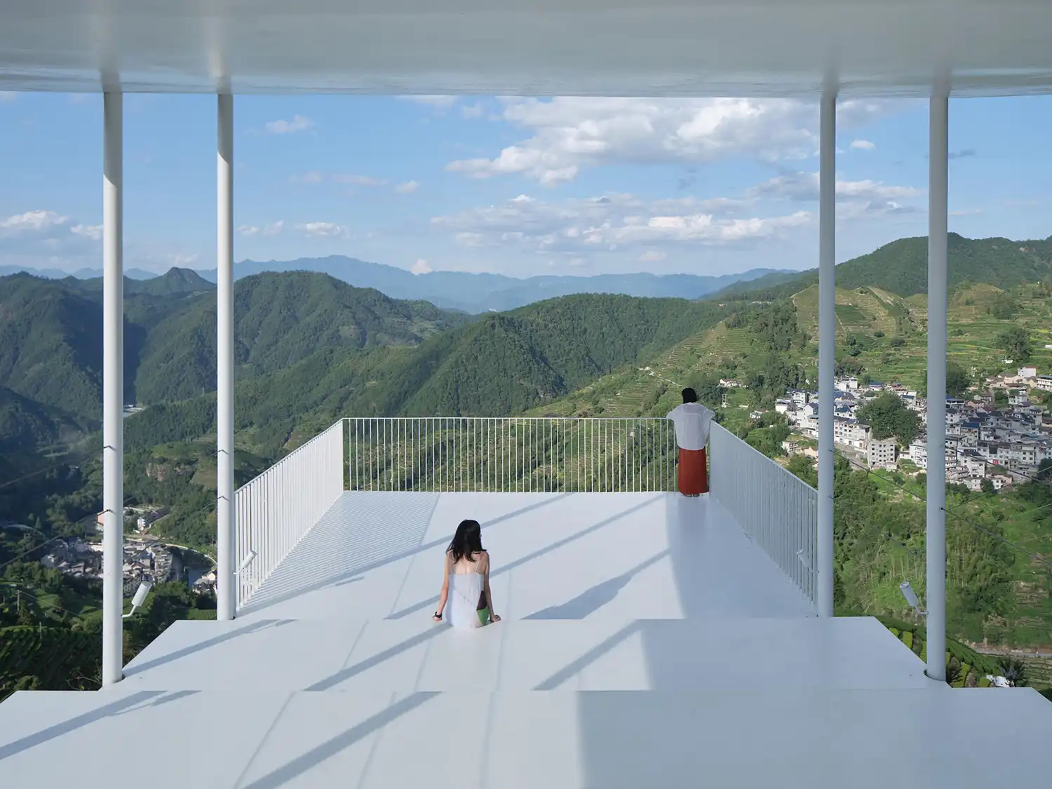 Interior view from the upper platform looking out toward distant blue mountains through the white pavilion structure.