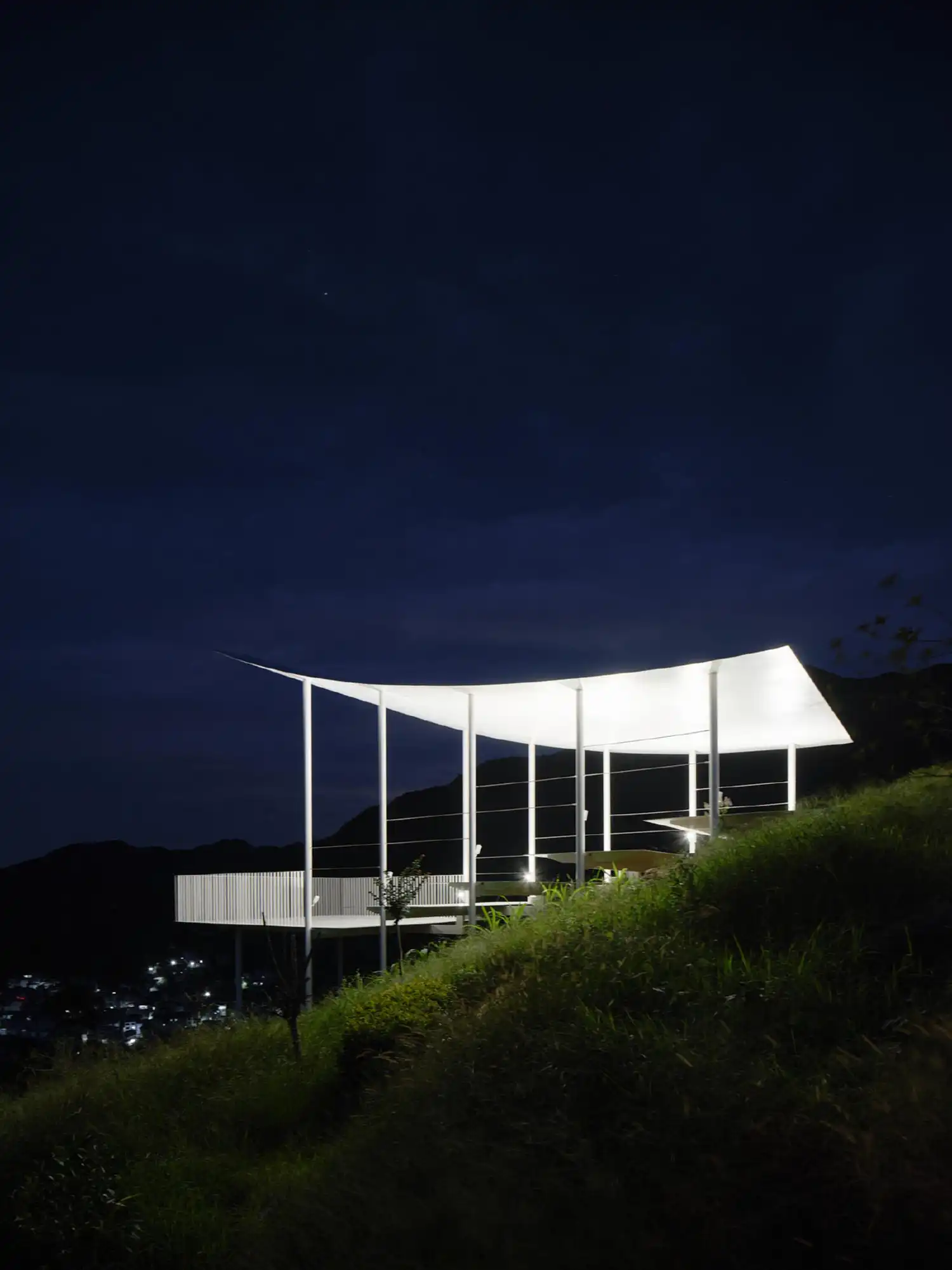 Night view of the Floating Pavilion with the curved roof soffit illuminated by upward-facing lights.