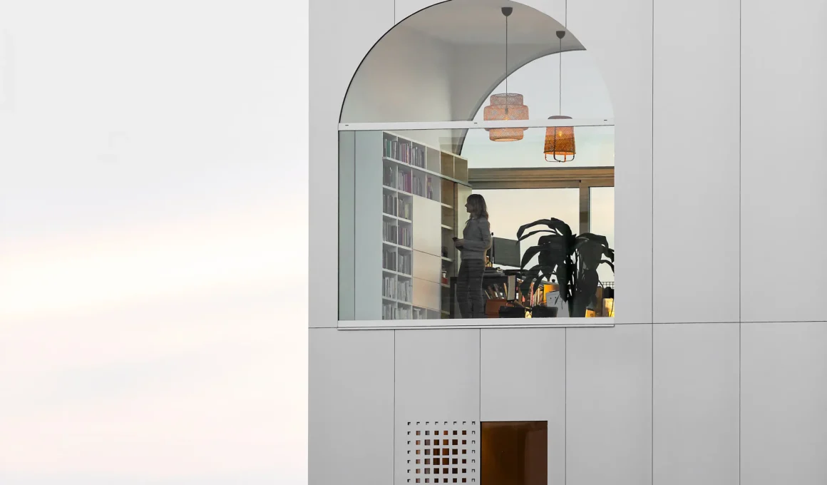 Close-up of an arched window on a grey facade showing a library and office interior.