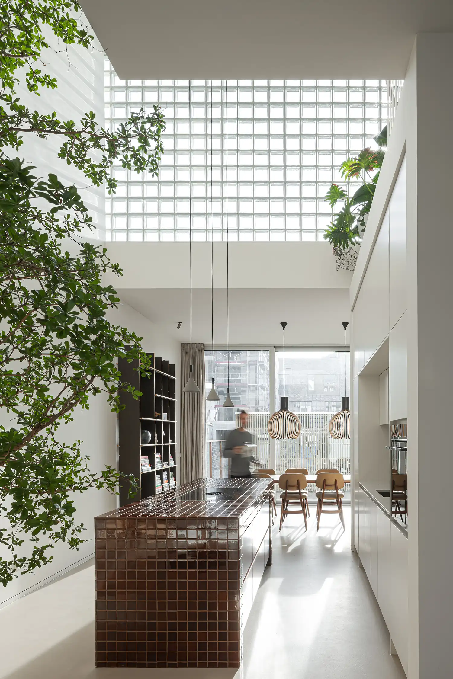 Interior of a double-height kitchen and dining area with glass block walls and brown tiled island.