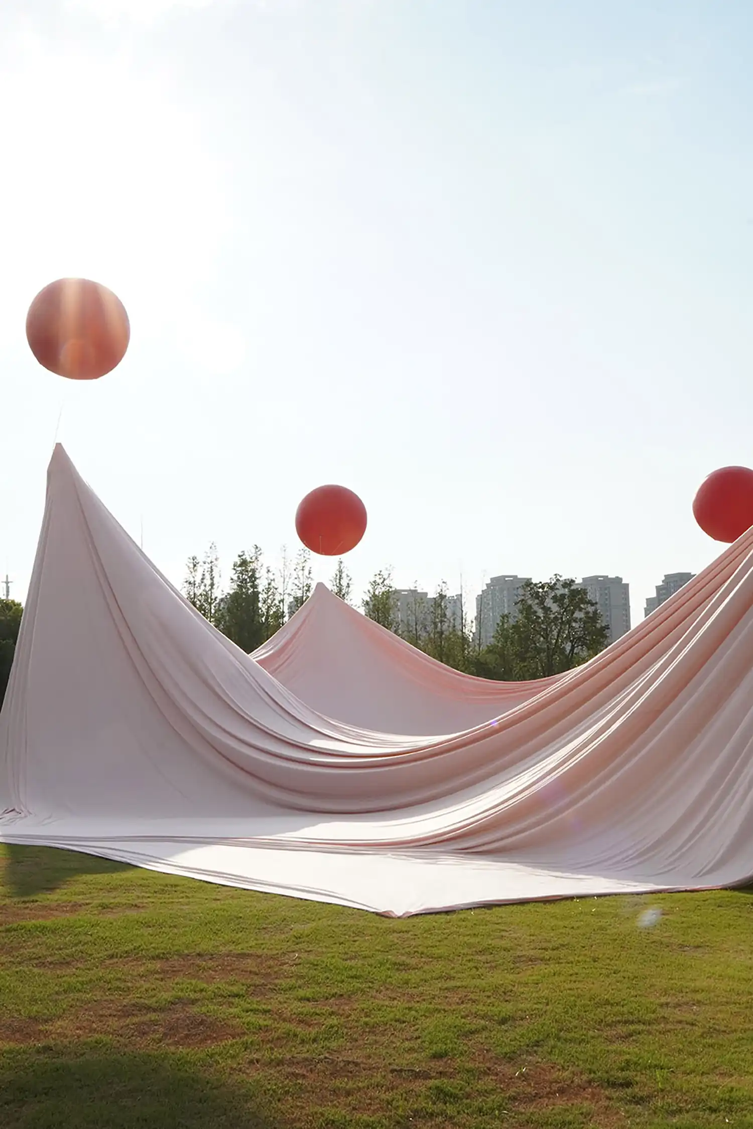 Rhythmic peaks of pink fabric against a sunny sky, topped with red balloons.