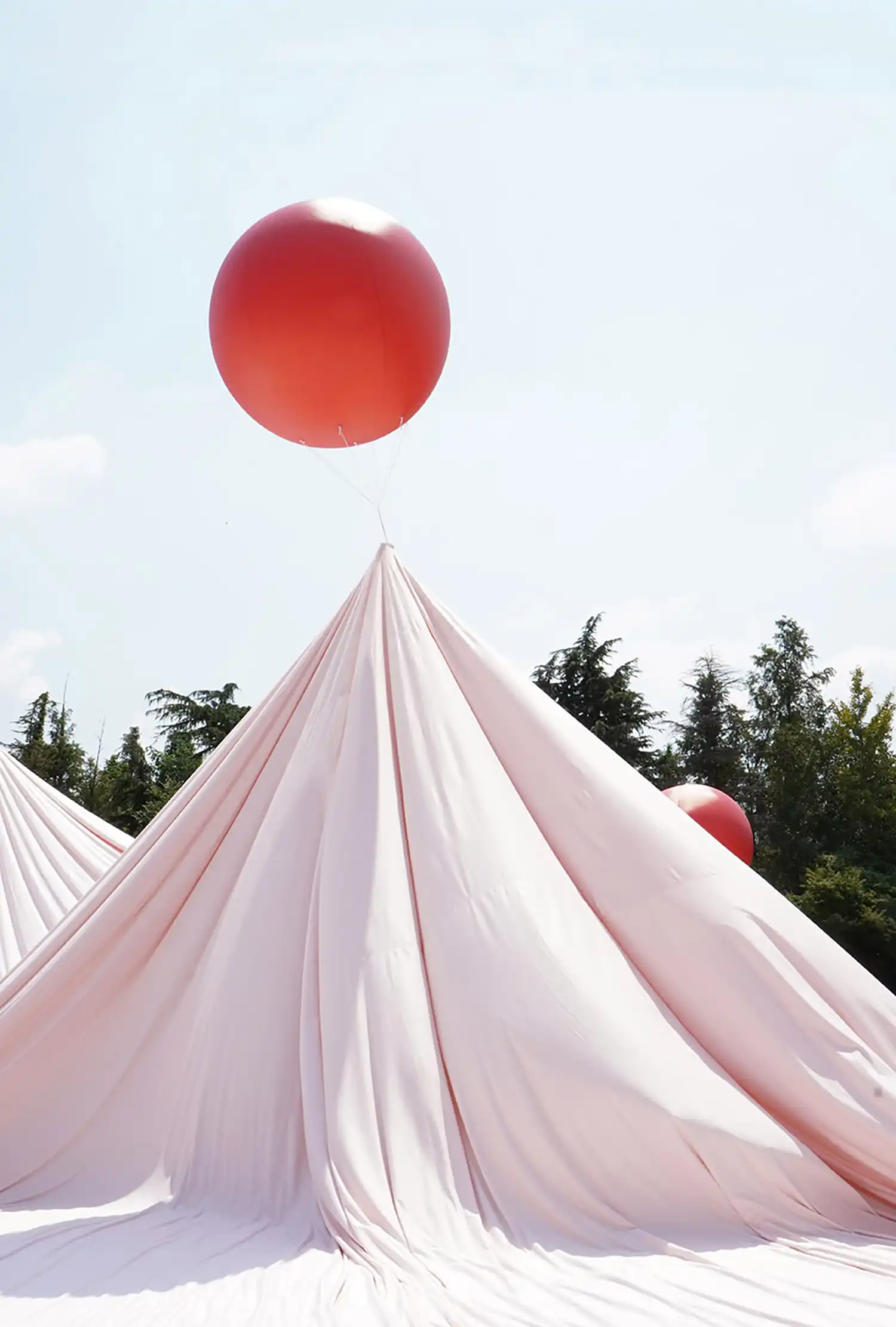 Vertical shot of a fabric peak pulled upward by a single red balloon into a clear sky.