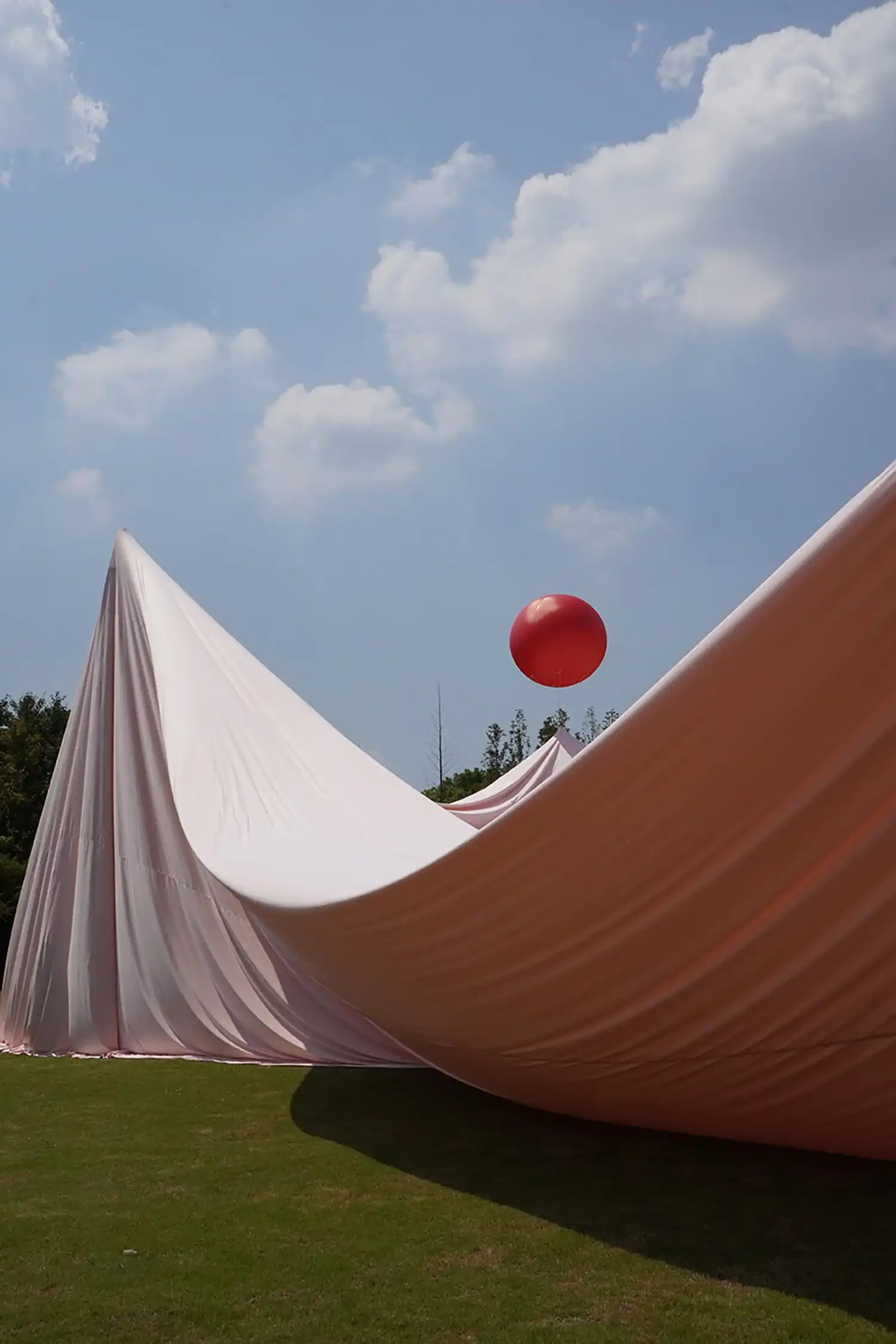 Dynamic curves of pink fabric dipping toward the grass with a red balloon in the background.