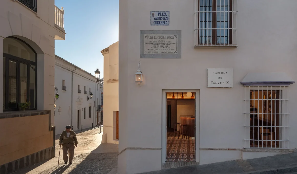 Street view of Taberna Convento entrance in El Viso del Alcor, Sevilla, with a man walking on a cobbled street.