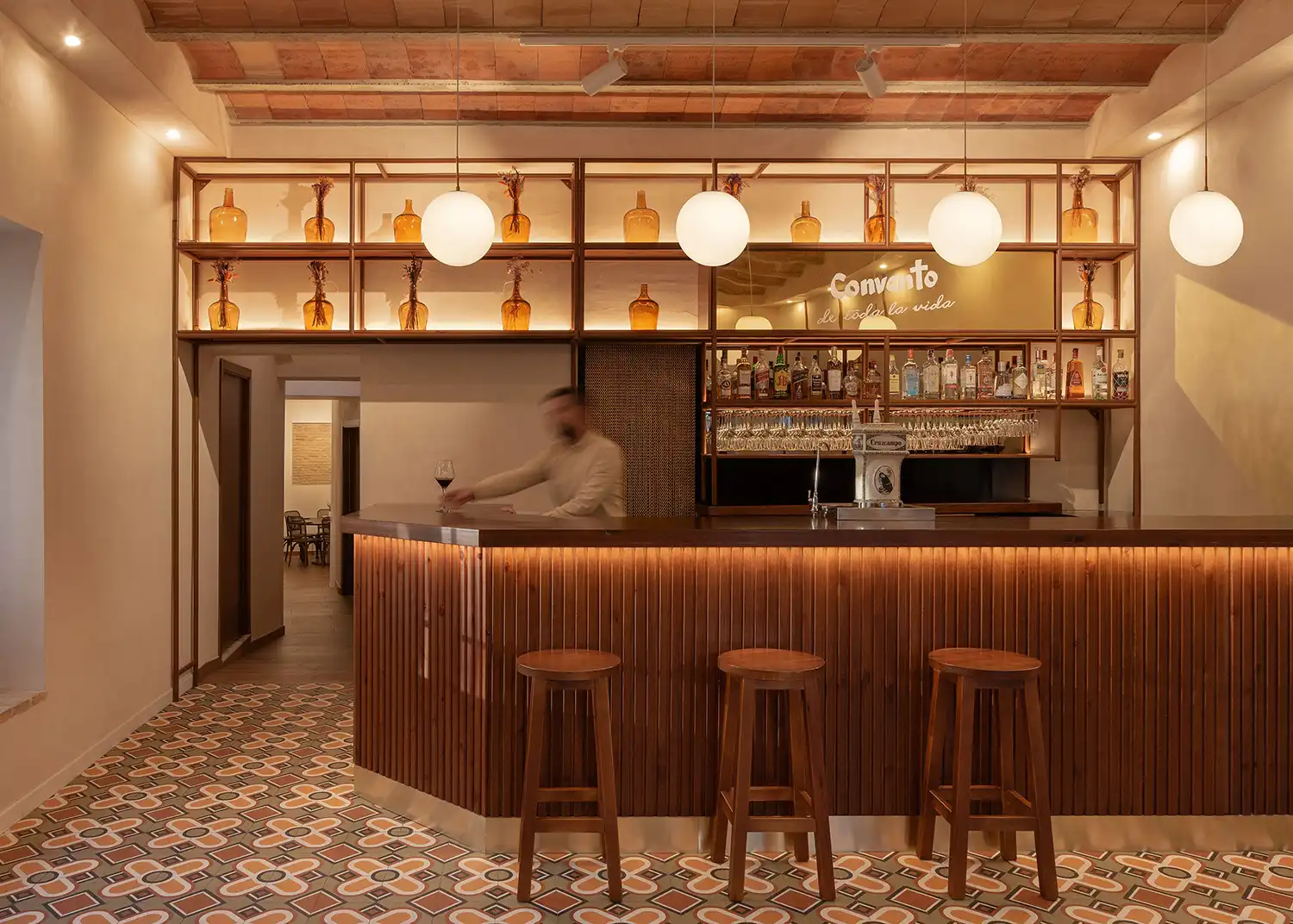 The internal bar area of Taberna Convento, showing the wooden bar counter, hydraulic tiles, and a bartender in motion.