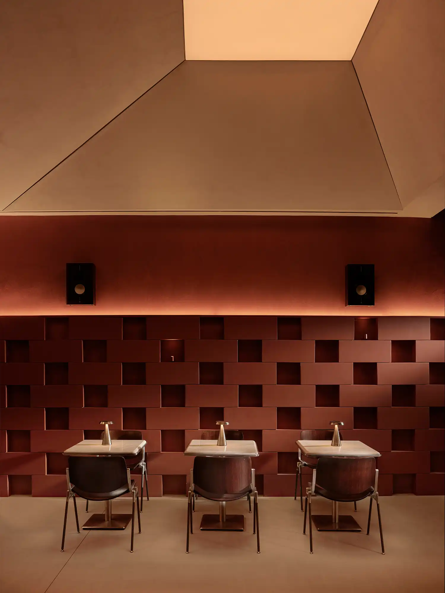 Symmetry of three dining tables with minimalist gold lamps under a geometric ceiling light.