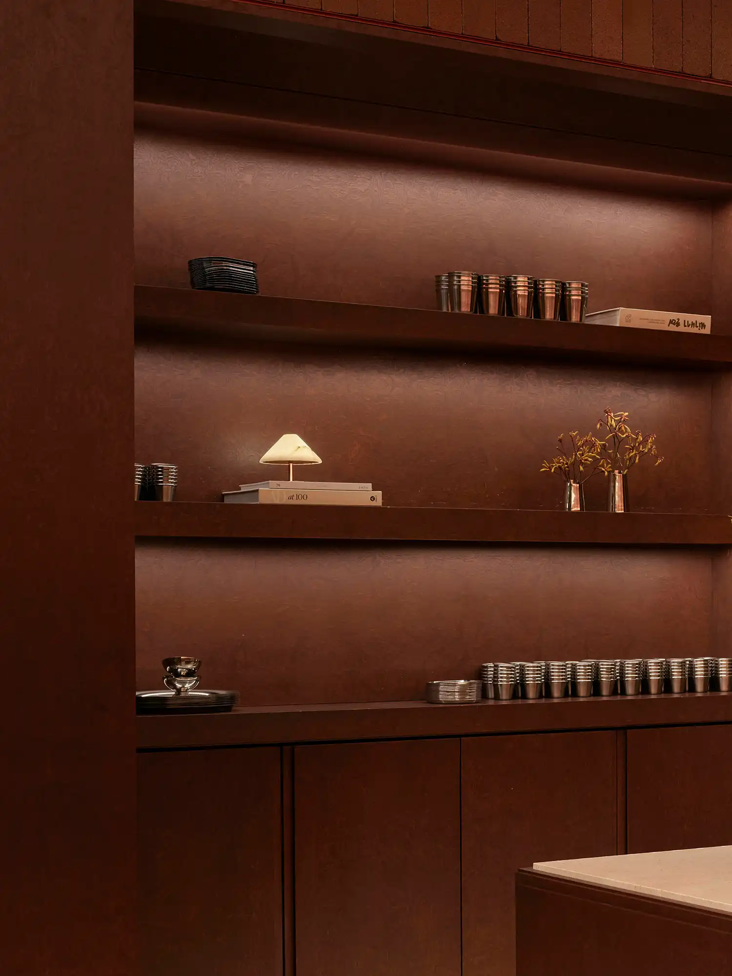 Close-up of lit recessed shelving with stainless steel cups and minimalist decor.