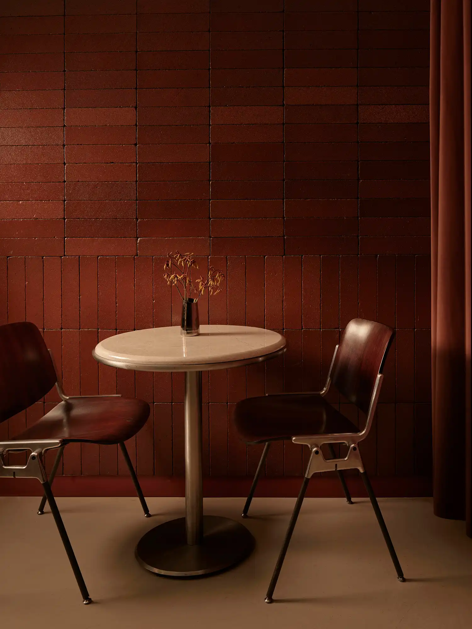 Round marble table and two Cassina chairs positioned against a vertical brick wall.