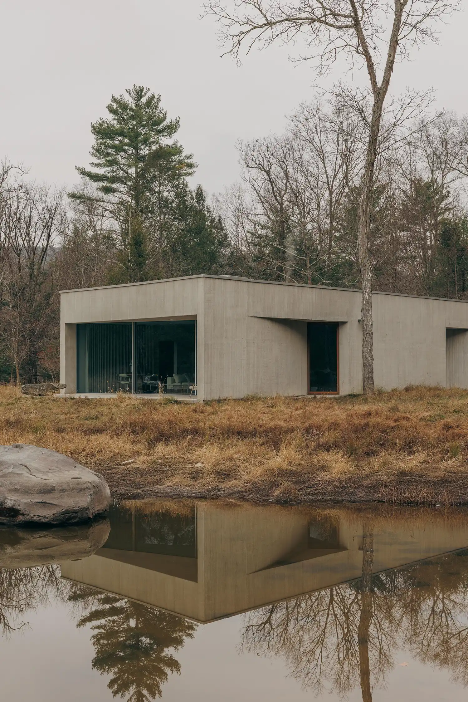 Exterior view of the Vipp Pavilion by Johnston Marklee, a rectangular stucco structure reflected in a still pond.