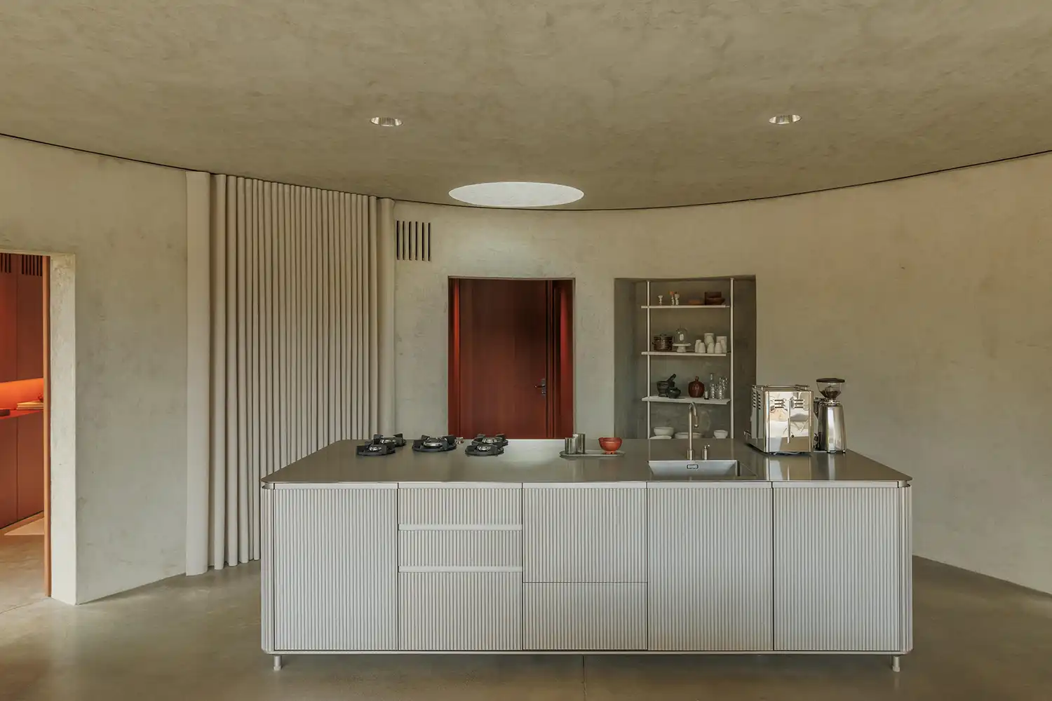 Modern kitchen island with a ribbed metal finish and integrated stovetop under a circular skylight.