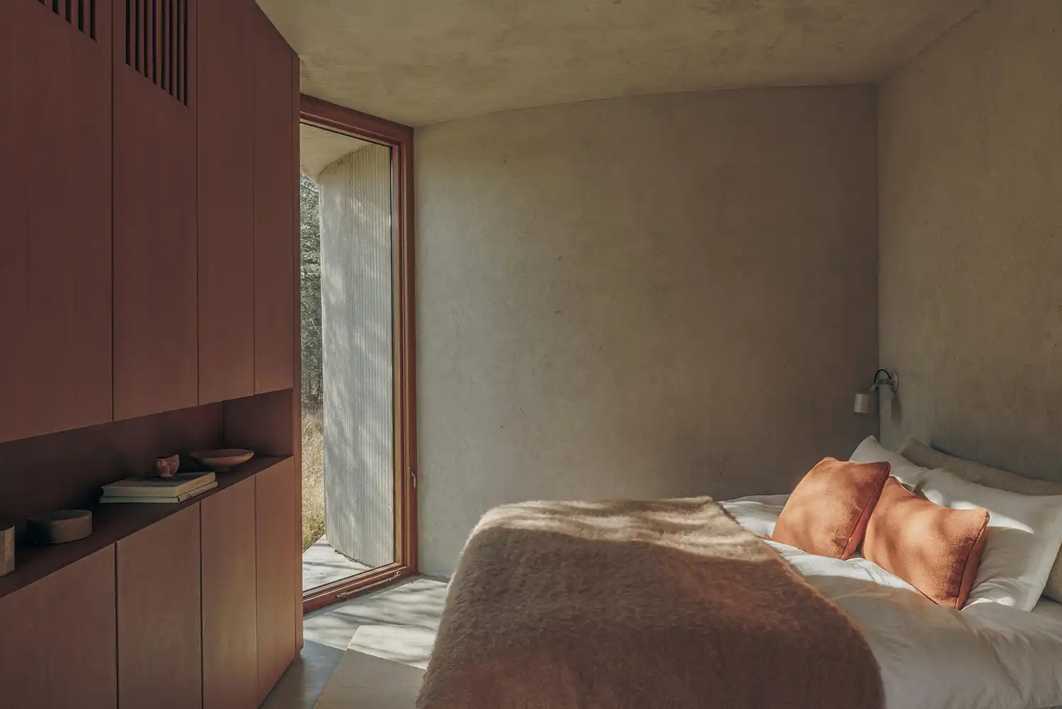 Minimalist bedroom with Sapele wood cabinetry and a floor-to-ceiling window looking out to the forest.