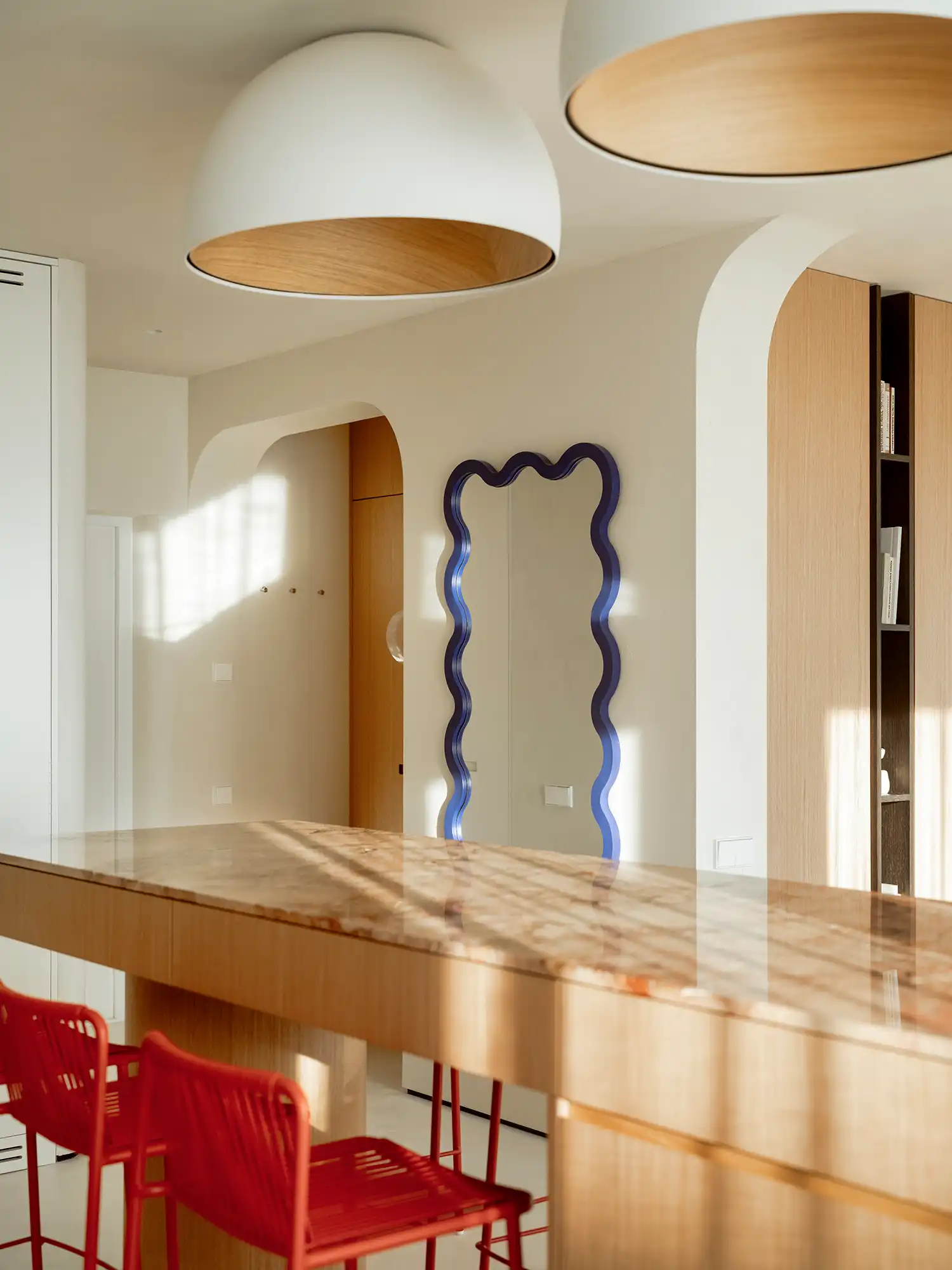 Marble kitchen island reflecting sunlight next to a blue wavy-edged mirror.