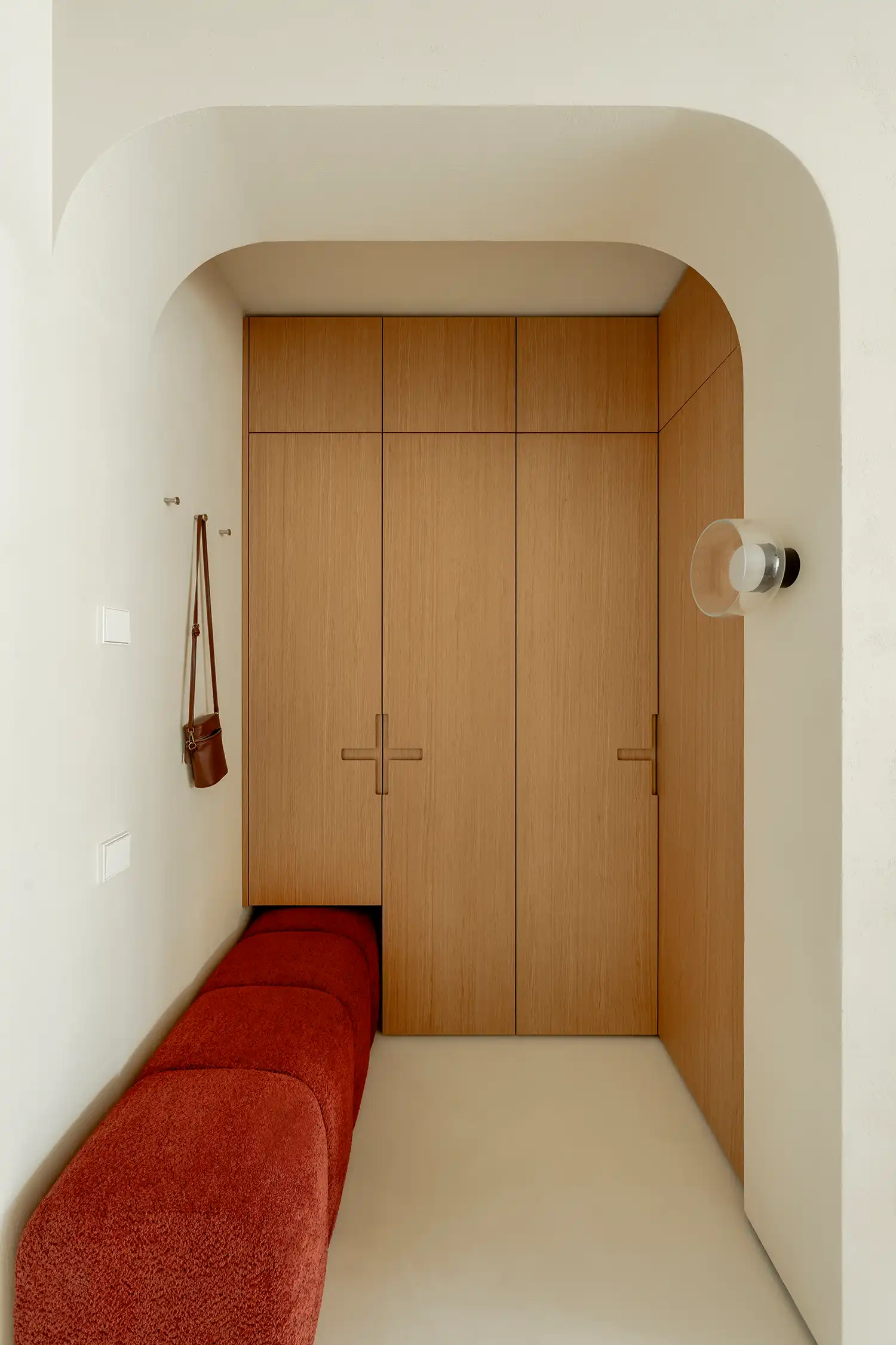 Entryway with light wood cabinetry, an arched opening, and a long red upholstered bench.