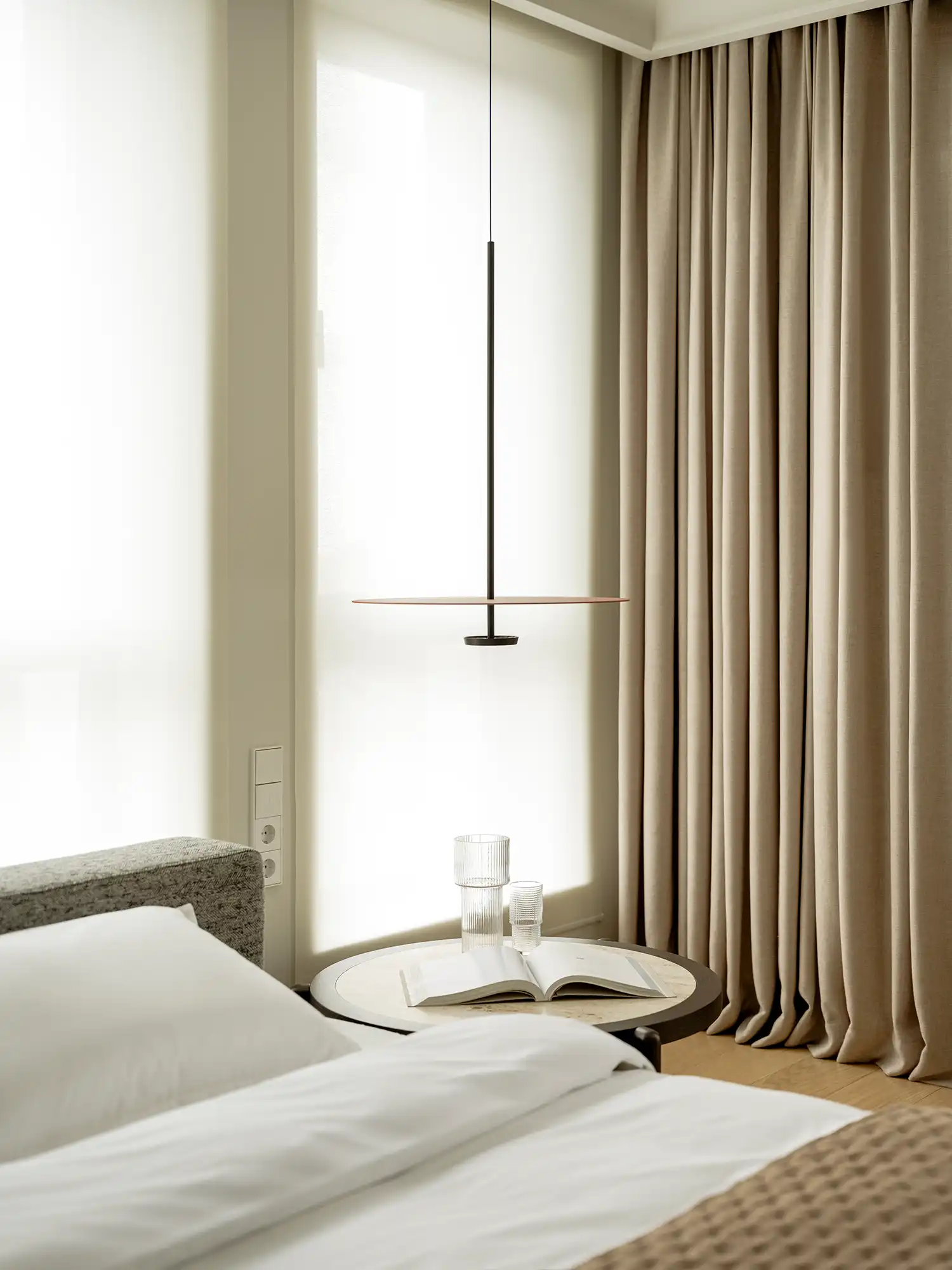 Serene bedroom with custom travertine side table and terracotta pendant light.