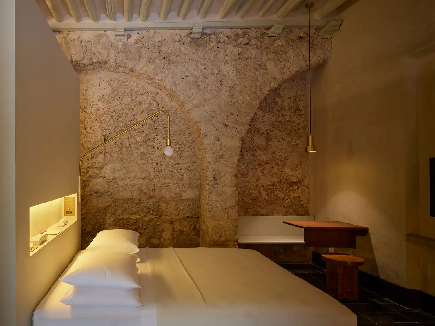 Minimalist bedroom at Hotel Sevilla with an original stone arch and custom wood furniture.