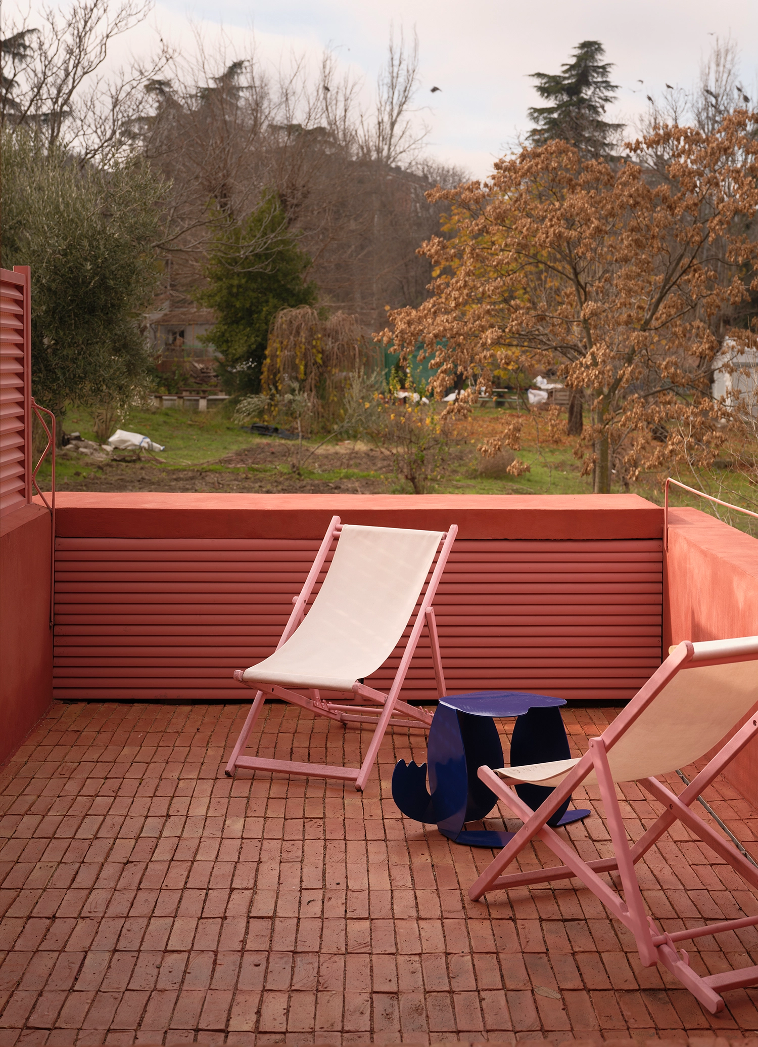 Rooftop terrace with red brick flooring, pink lounge chairs, and a view over a wooded Madrid neighborhood.