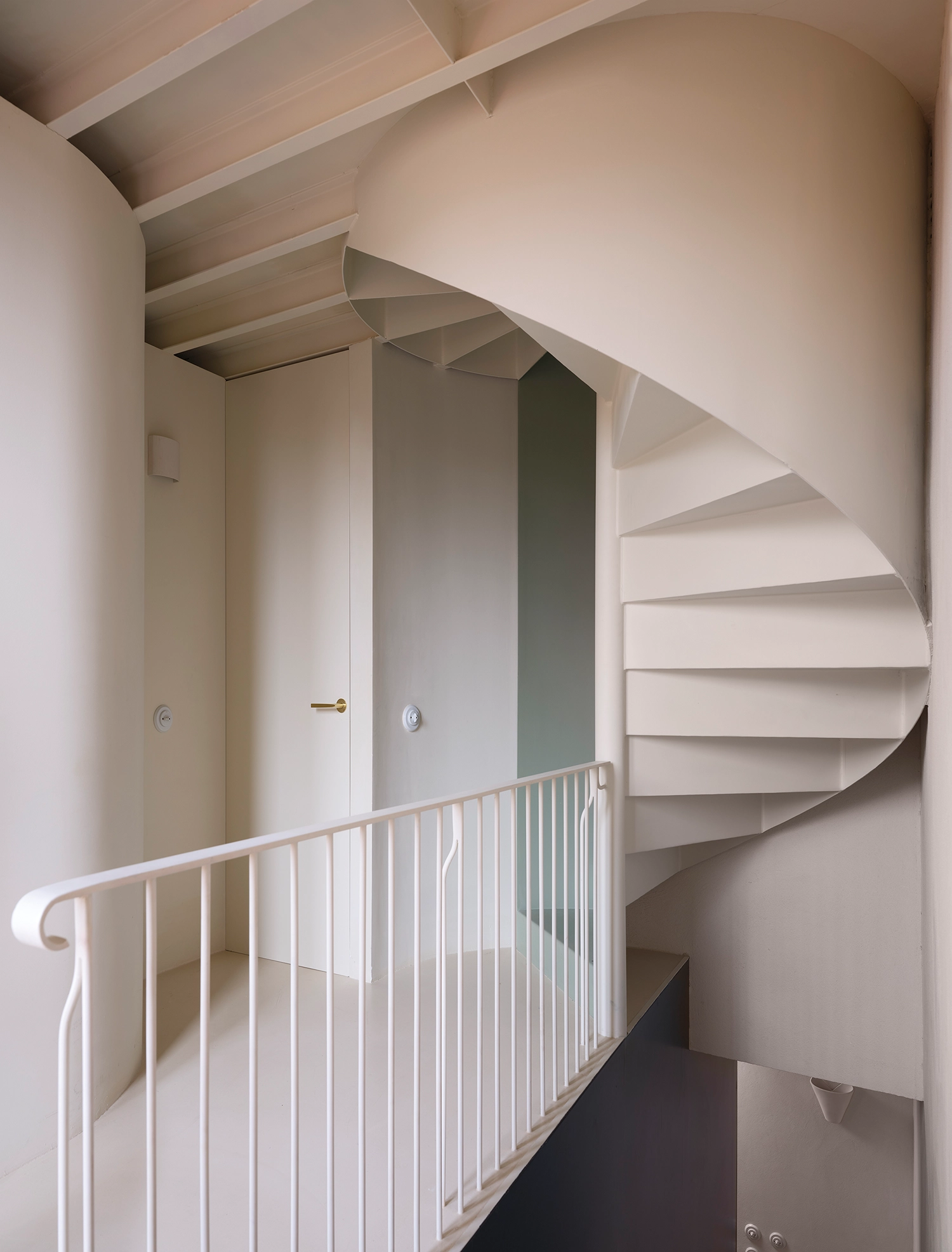 Interior view of a minimalist white spiral staircase leading to an upper floor under exposed steel beams.