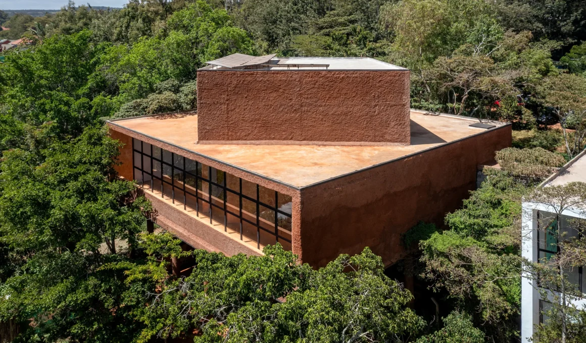 Aerial view of a monolithic red earth-plastered building nestled in a dense green forest in Nairobi.