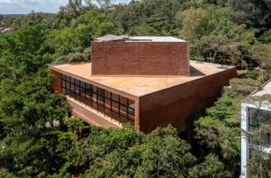 Aerial view of a monolithic red earth-plastered building nestled in a dense green forest in Nairobi.