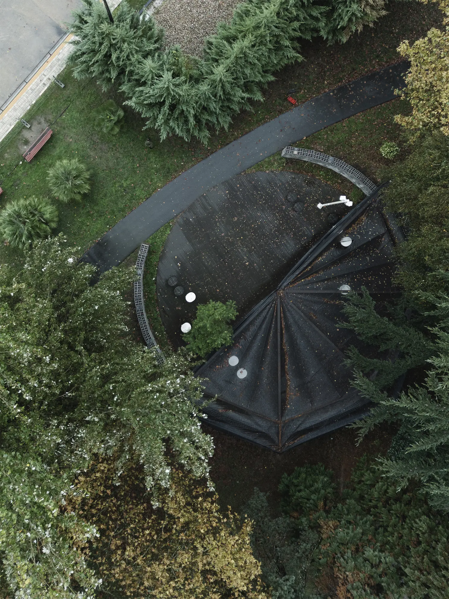 An aerial photograph showing a top-down view of the circular Rotação pavilion by Atelier Tiago Antero, surrounded by the foliage of diverse trees in the Quinta da Capela garden.
