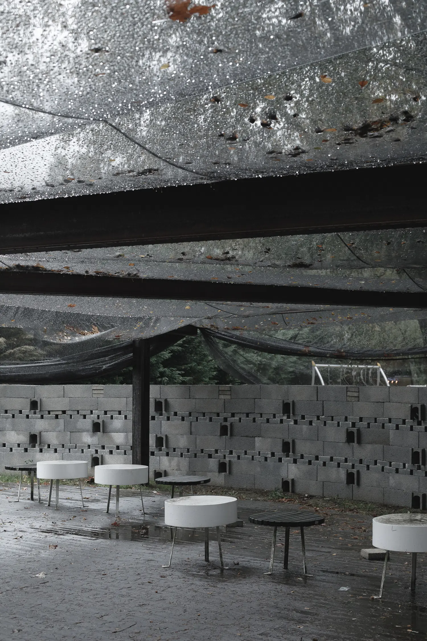 A wide-angle interior photograph of the circular Rotação pavilion by Atelier Tiago Antero, showing the curved concrete block wall and numerous minimalist stools on the wet pavement.